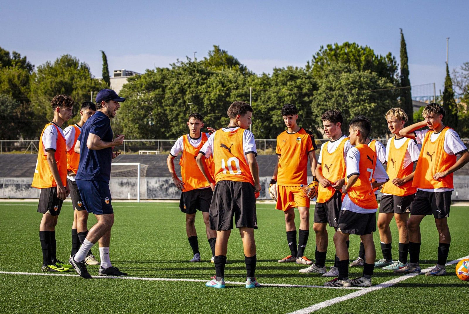 A coach and young footballers during a training session on a football pitch in Spain
